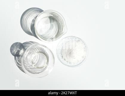 Closeup chemical ingredient on white laboratory table. Di-Ammonium Prosphate in Chemical Watch Glass place next to beaker with alcohol and Erlenmeyer flask. Top View Stock Photo