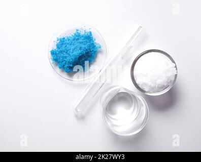 Copper(II) sulfate in Chemical Watch Glass, Crystal clear liquid in beaker and Microcrystalline wax in glass container placed next to Test tube. Top view Stock Photo