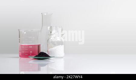 Cosmetic chemicals ingredient on white laboratory table. Potassium Permanganate Liquid in beaker, KMnO4 in chemical watch glass and Microcrystalline wax in glass container. Stock Photo