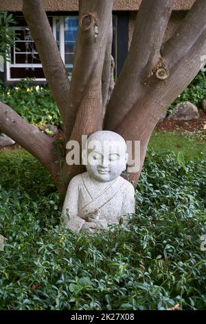 Granite sculpture of a Buddha and a rabbit sitting under a tree surrounded by greenery Stock Photo