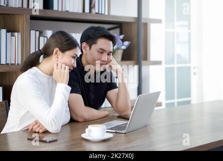Asian couples spend time together in the living room. Both had a serious expression on their faces after seeing a quote for a home improvement. Stock Photo