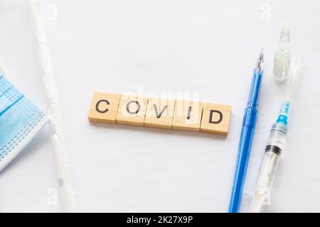 The inscription covid on a medical background, next to the vaccine, syringe, pen, protective mask. Medical theme. Concept: vaccination against coronavirus. Stock Photo