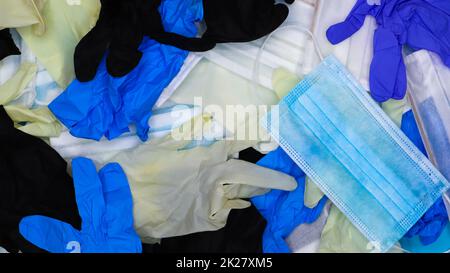 Multicolored crumpled latex surgical gloves and medical protective masks lie in disarray. Flat lay. Used remedies against the Covid-19 virus Stock Photo