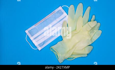 A pair of disposable latex medical gloves and a surgical mask on a blue background. Covid-19 virus protection concept. Protective items. Means of protection. Stock Photo