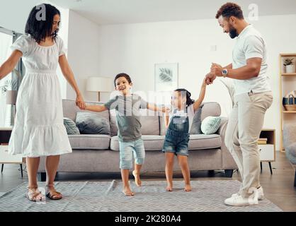 Happy family, dancing and having fun while sharing love, energy and bond while holding hands in the living room at home. Man, woman and sibling kids Stock Photo