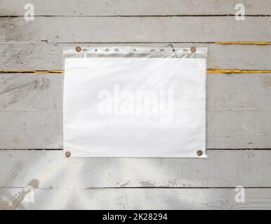 White paper sign with rivets, vintage background on a gray wooden old backdrop. Wooden textured wall, weighs a white blank cardboard sign lit by the sun, closeup Stock Photo