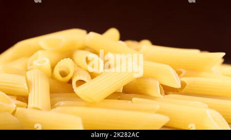 Penne Rigate Raw Pasta is a short pasta with oblique cuts and a ribbed surface. Traditional Italian pasta. Pasta background. Italian food ingredient side view. Stock Photo