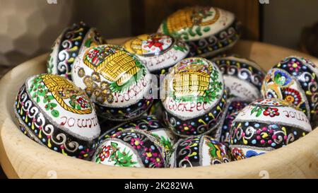 Ukraine, Bukovel - November 20, 2019: Easter eggs in a wooden plate with the text Christ is Risen. Ukrainian traditional hand painted easter eggs. Souvenirs on the window, wooden ovals. Stock Photo