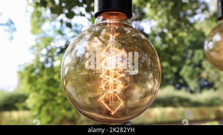 Edison incandescent bulbs hang in a retro loft style. Cafeteria decoration close-up. Street decor Light lanterns Warm light. Soft focus, blurred street background Stock Photo