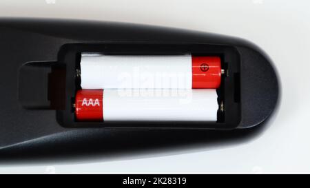 Black TV remote control with AAA alkaline batteries in red and white on a white background. Battery replacement, spare parts. Remote control battery compartment close-up. Stock Photo
