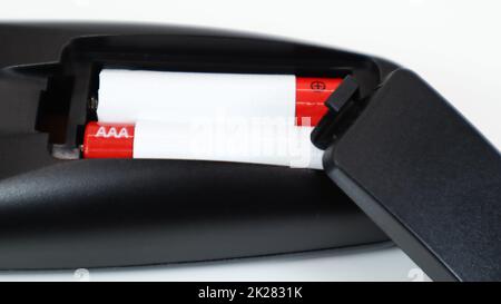 Black TV remote control with AAA alkaline batteries in red and white on a white background. Battery replacement, spare parts. Remote control battery compartment close-up. Stock Photo