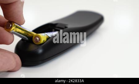 Insert the AAA size battery into the remote control. Installing batteries in the wireless device. A male hand holds a yellow alkaline battery. Text in English and Russian. Stock Photo