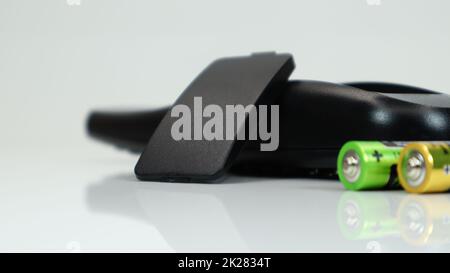 Black TV remote control with AAA alkaline batteries on a white background. Battery replacement, spare parts. Close up of the battery compartment of the remote control. Stock Photo