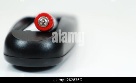 Black TV remote control with AAA alkaline batteries on a white background. Battery replacement, spare parts. Close up of the battery compartment of the remote control. Stock Photo