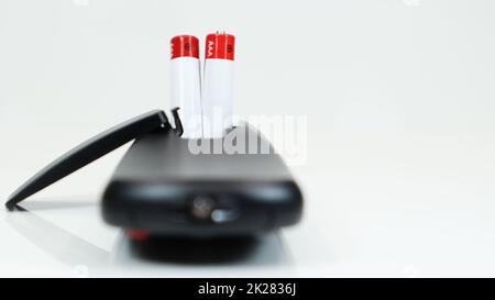 Black TV remote control with AAA alkaline batteries on a white background. Battery replacement, spare parts. Close up of the battery compartment of the remote control. Stock Photo