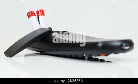 Black TV remote control with AAA alkaline batteries on a white background. Battery replacement, spare parts. Close up of the battery compartment of the remote control. Stock Photo