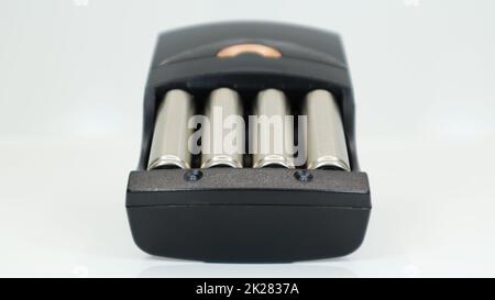 Rechargeable alkaline batteries in a battery charger on a white background. AA fast charger in black. The battery is charging. Stock Photo