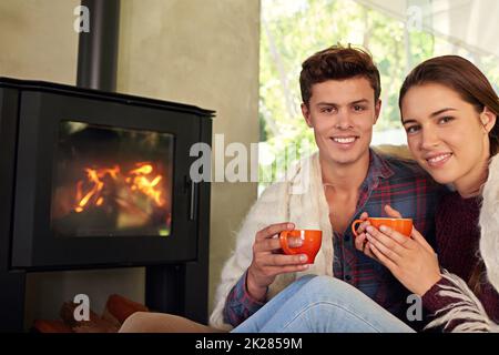 Hold on to whatever keeps you warm. a young couple drinking hot chocolate by the fireplace. Stock Photo