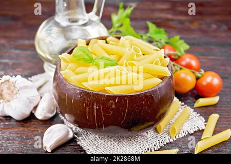 Penne in bowl of coconut with vegetables on wooden board Stock Photo