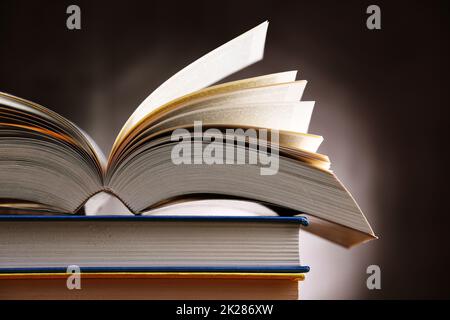 A composition with an open book lying on a stack of other books Stock Photo