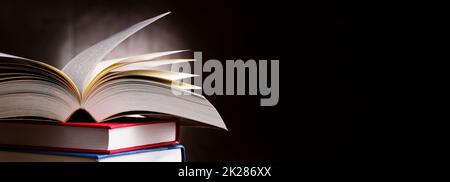 A composition with an open book lying on a stack of other books Stock Photo