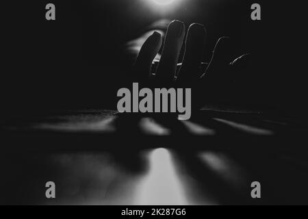 A woman's hand in the dark lies on the ground in the light of a lantern, black and white photo, fear and horror, hand Stock Photo