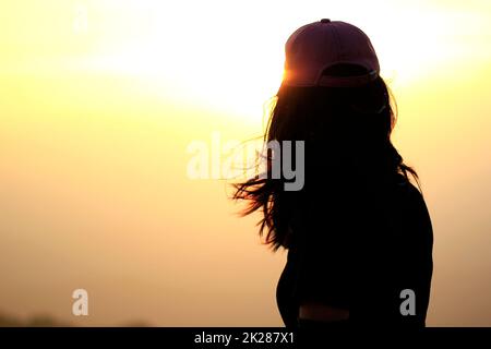 woman wearing a hat standing on the mountain Admire the beautiful landscape of the evening sunset. Stock Photo