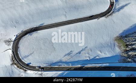 Aerial drone shot of snowy landscape with curvy road with cars Stock Photo