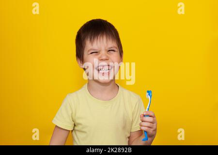 Happy toddler boy brushing his teeth with a toothbrush on a yellow background. Health care, oral hygiene. Stock Photo