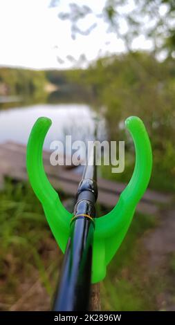Fishing rod feeder on a stand against a lake. Close fishing on the river, fishing rod stands on a green slingshot Stock Photo