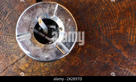 Metal ashtray on a brown wooden table top view. Smoking in public places. Flat lay. Stock Photo