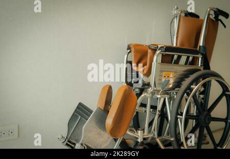 Empty wheelchair near wall in hospital for service patient and people with disability. Medical equipment in hospital for assistance old people. Chair with wheels for patient care in nursing home. Stock Photo