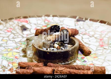Homemade cigars from leafy tobacco leaves on a ceramic table. Ashtray and cigars. Stock Photo