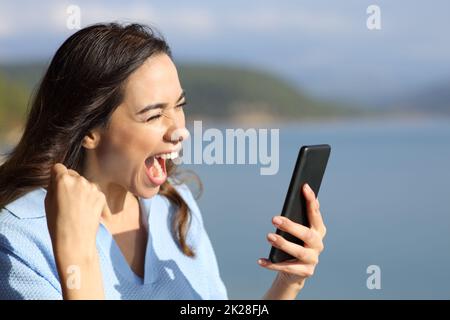 Excited woman in a lake checking phone on vacation Stock Photo