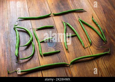 The word beans made from pods on a wooden table. Plantation work. Autumn harvest and healthy organic food concept close up with selective focus Stock Photo