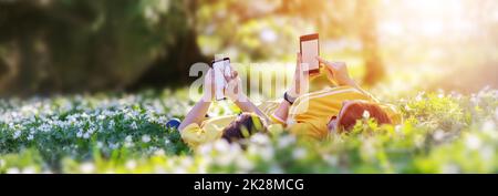 Mother and her son lying down with phones on the meadow in the park Stock Photo