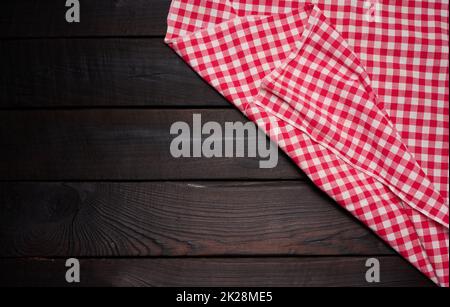 folded red and white cotton kitchen napkin on a wooden brown background, top view, copy space Stock Photo
