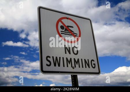 The No Swimming sign with the icon and a blue and white sky behind Stock Photo