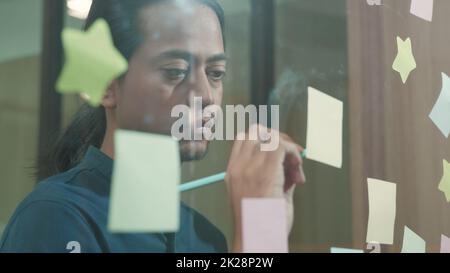 Businessman sticking adhesive notes on glass wall in creative in office Stock Photo