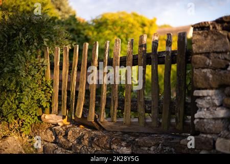 Old wooden picket fence built into a wall from stones. Stock Photo