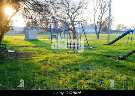 Children's playground near the stadium on the background of sunset. Swings, slide and ladder. Carousel and shop. Leisure for children. Children playground. Swings and a slide to slide Stock Photo