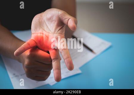 The man stretches his ring finger after he has worked. Office syndrome concept. Pain symptom area is shown with red color. Close up shot. Stock Photo