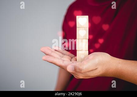 Valentine's day concept. Someone holds wood blocks that shows levels of Love from up to down, more to less, respectively. White heart shape is designed in visual effect form. Stock Photo