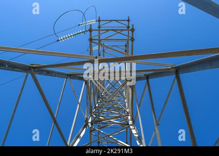 Supports high-voltage power lines against the blue sky. View from the bottom up Stock Photo