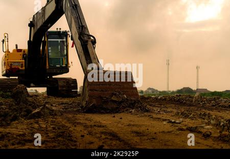 Backhoe parked at construction site after digging soil. Closeup bucket of bulldozer. Digger after work. Earth moving machine at construction site of housing estate. Digger with dirt bucket and soil. Stock Photo
