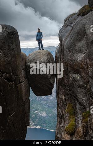 Woman stands on top of large boulder, Visiting Norway Kjeragbolten located south of Lysefjorden Stock Photo