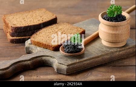 fresh grainy black paddlefish caviar in brown wooden spoon on a brown table, close up Stock Photo