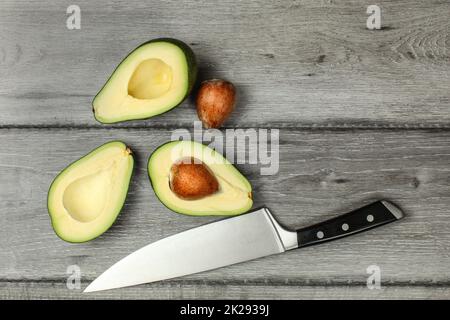Tabletop view, two avocados cut in half, seeds visible, with chef's knife next to them. Stock Photo