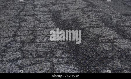 Close-up view of an old asphalt road in wet cracks. Worn road with cracks texture. Stock Photo