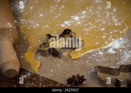 On the parchment there is a carver in the form of a man near the rolled dough, everything is sprinkled with flour, a rolling pin and other molds are visible, a photo in a dark key Stock Photo